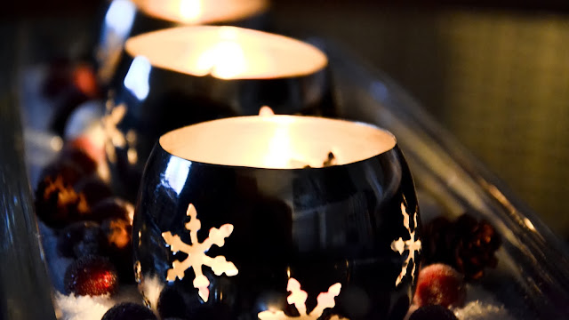 Carved linocut relief print of glossy candle holders glowing warmly, decorated with soft snowflake shapes, deep and golden tones
